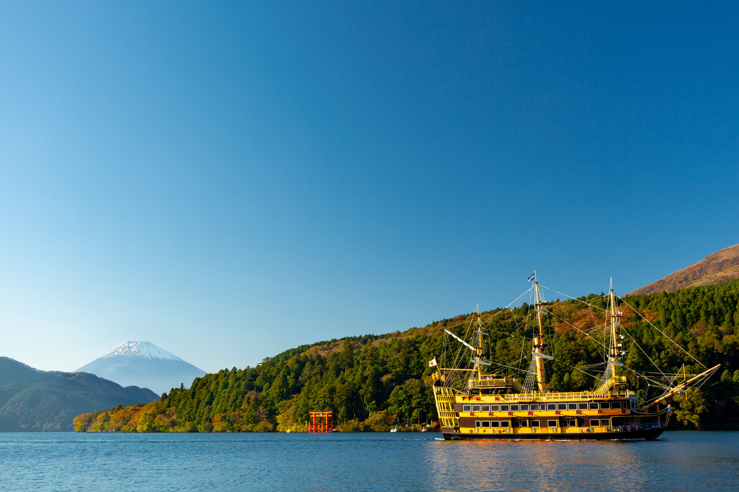 Golden Hakone pirate ship on Lake Ashi in autumn, with snow-capped Mount Fuji and the red torii gate of Hakone Shrine