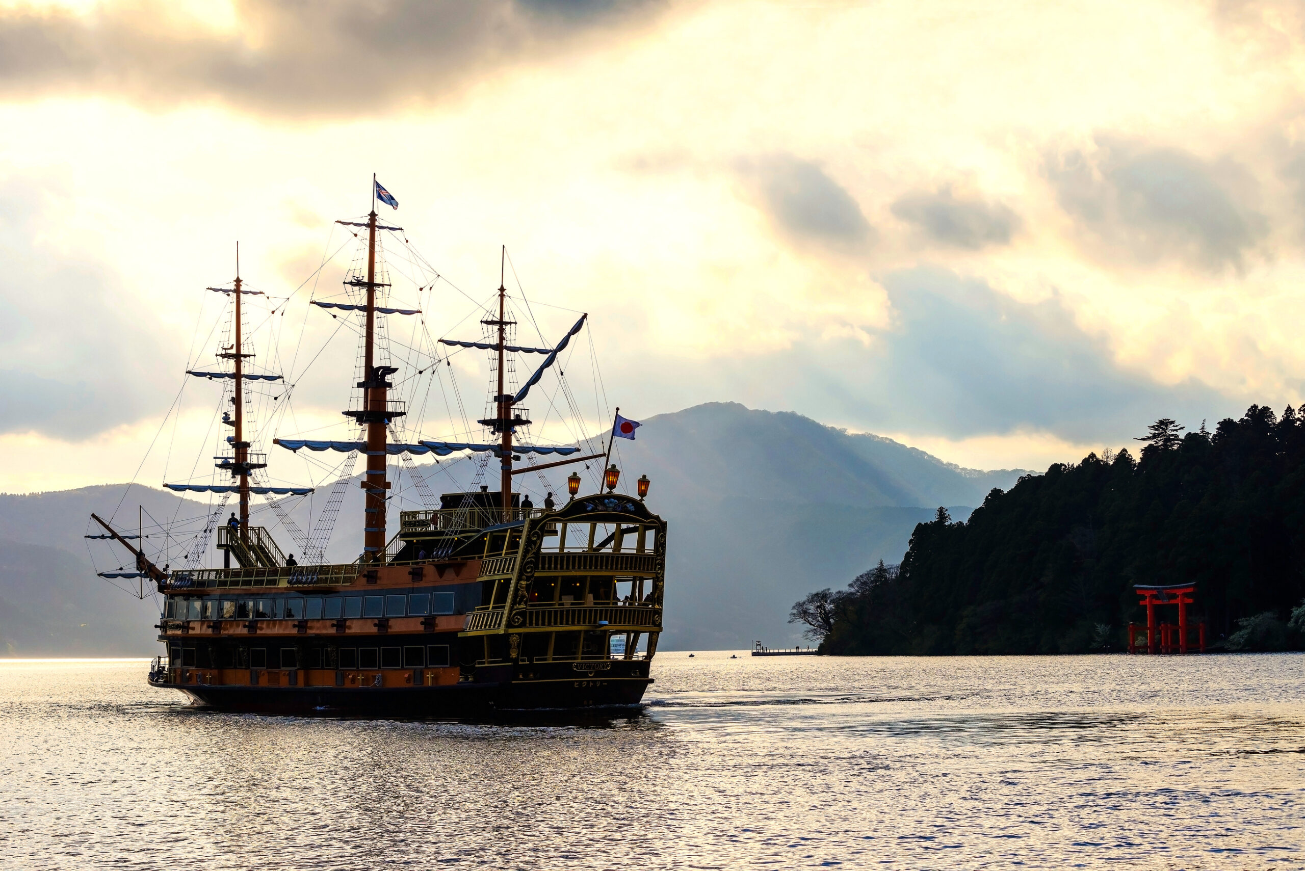 Pirate ship crossing Lake Ashi at dusk, with Hakone Shrine's red torii gate on the far shore