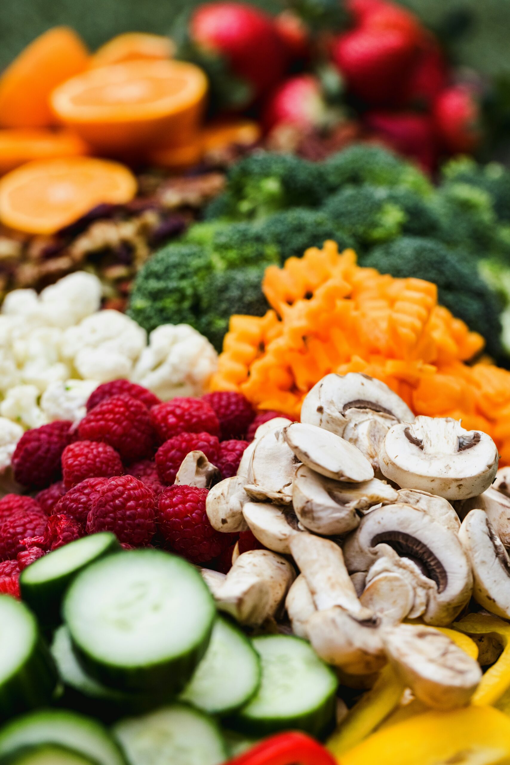 Close-up of a variety of fresh vegetables and fruits, including mushrooms, cucumbers, raspberries, and broccoli, showcasing vibrant colors.