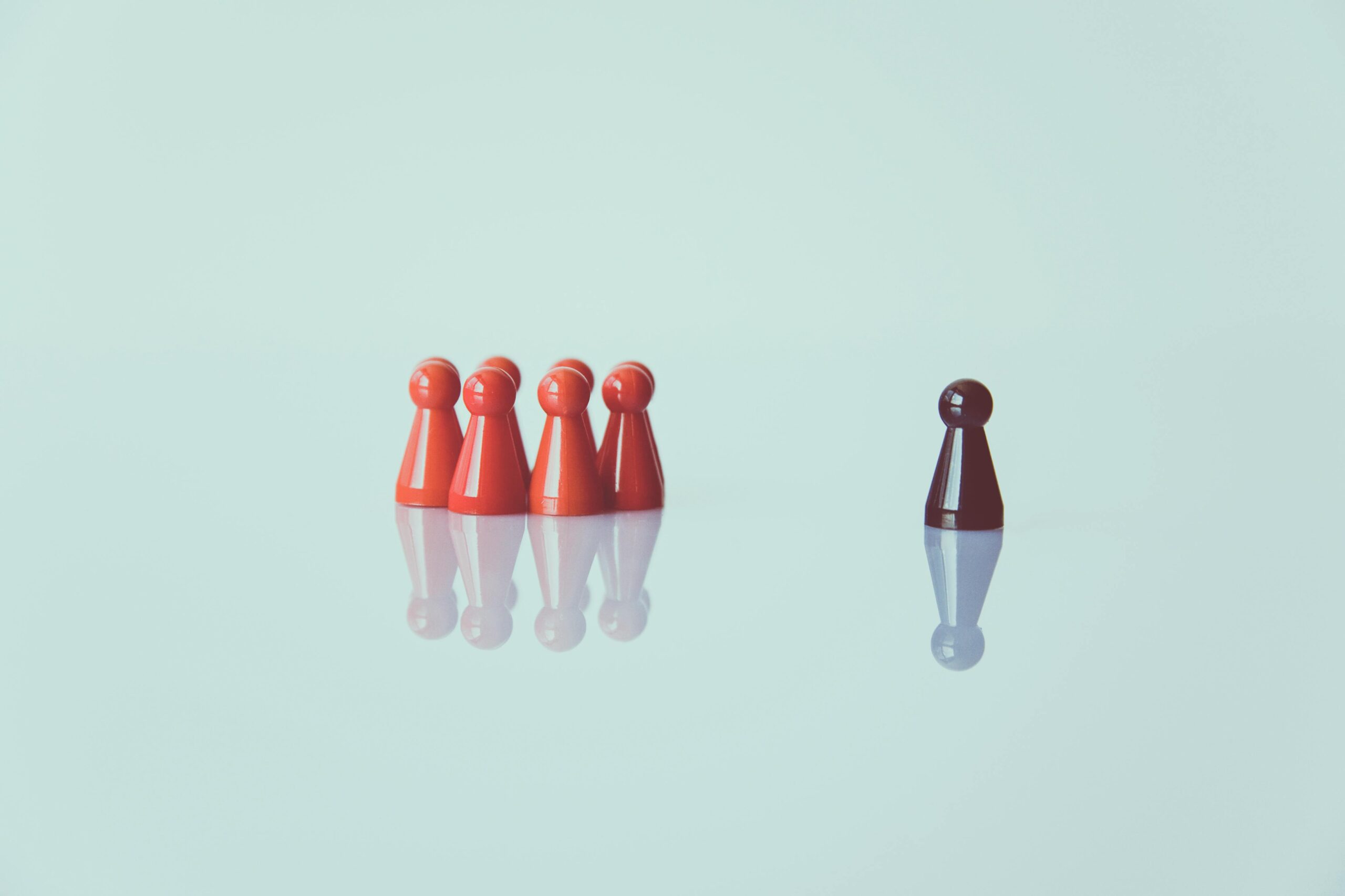 A group of red chess pieces on the left, contrasted by a lone black chess piece on the right, symbolizing the loneliness one can feel when they don’t fit in with their surroundings.