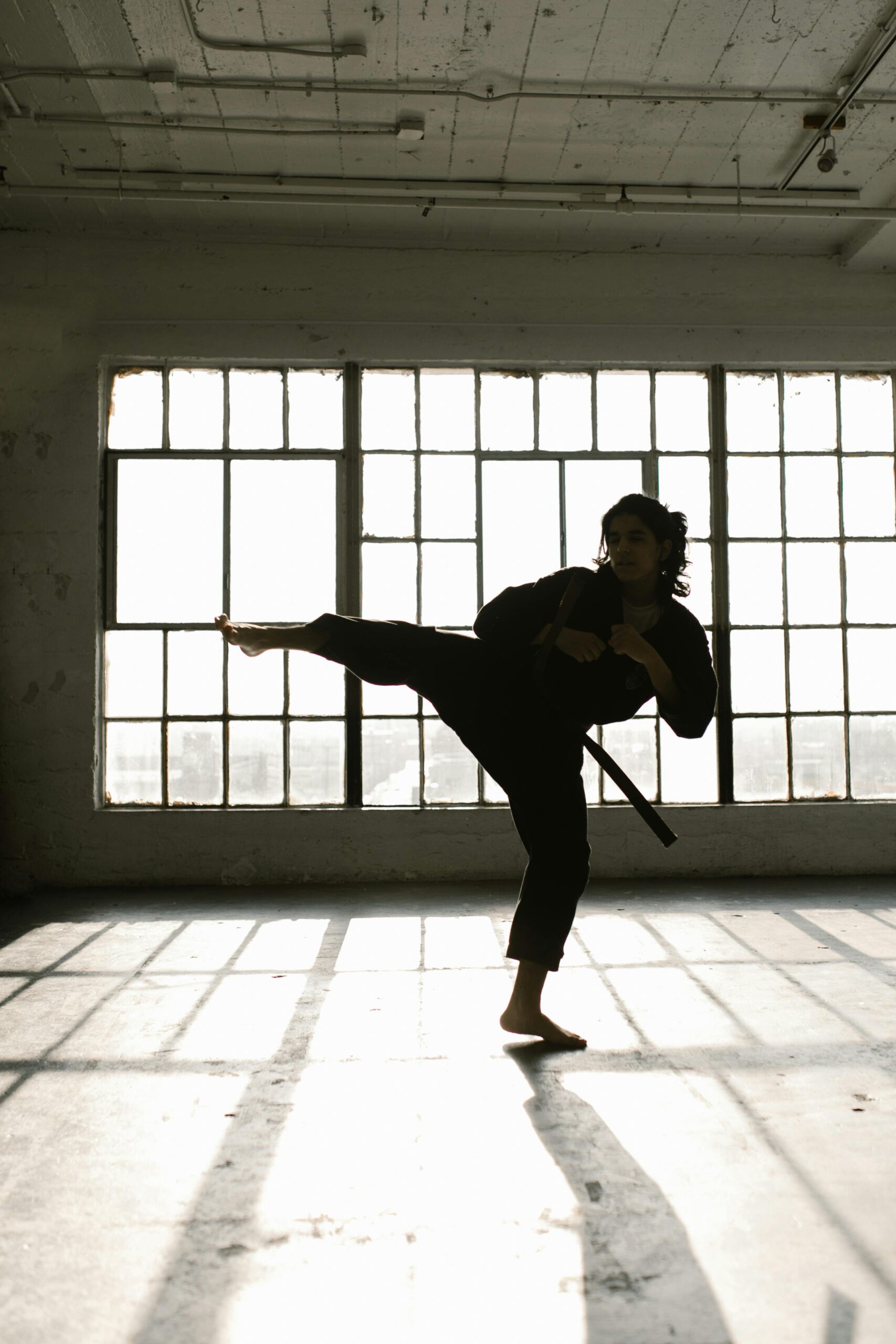 Woman in a karate uniform performing a high kick, demonstrating strength and precision in martial arts.