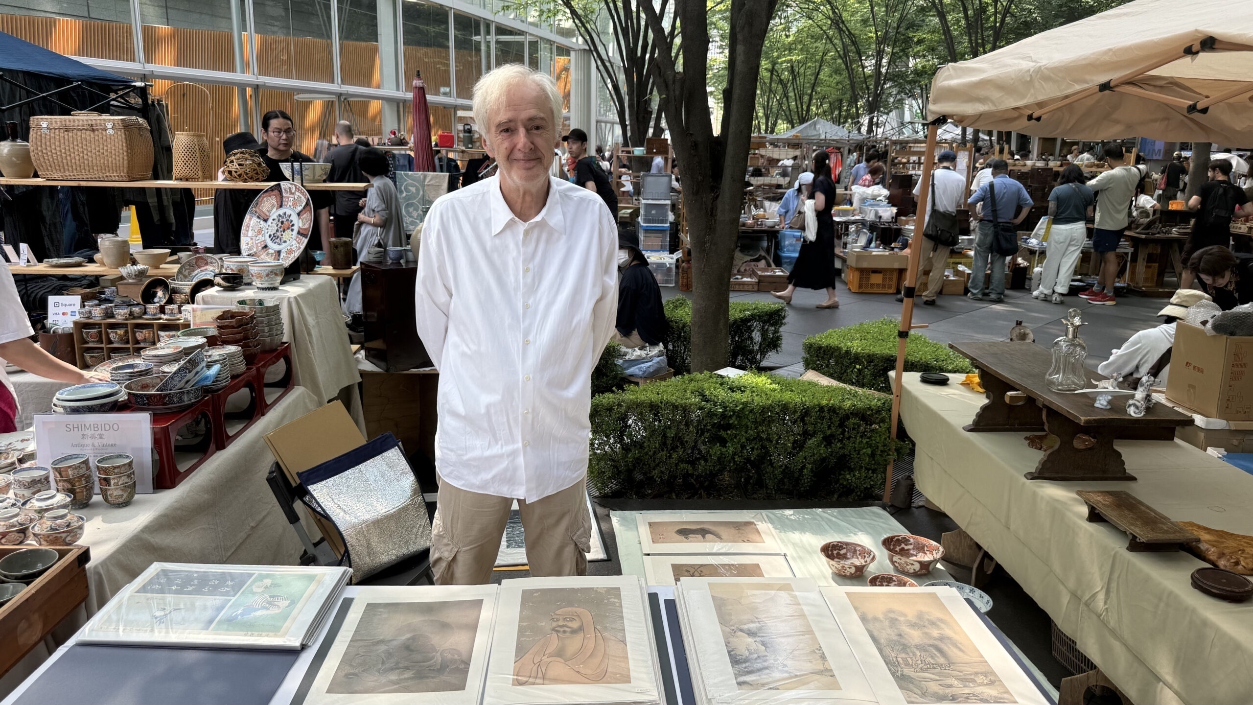 A stall selling ukiyo-e woodblock prints and art at the Oedo Antique Market, with browsing shoppers and greenery behind